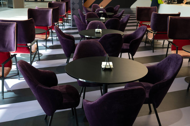 A row of tables with soft comfortable violet chairs for visitors to the food court of a modern shopping center. People admire the beautiful view during the meal. - Fotó, kép