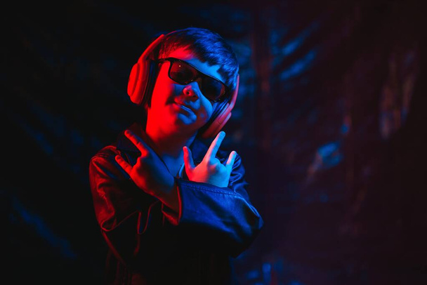 teen boy listening to music with headphones, neon light trending portrait. Looks at the camera - Фото, изображение