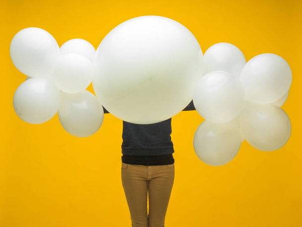 junge Brünette mit weißen Luftballons in den Händen vor ihrem Kopf auf gelbem Hintergrund Verkauf - Foto, Bild