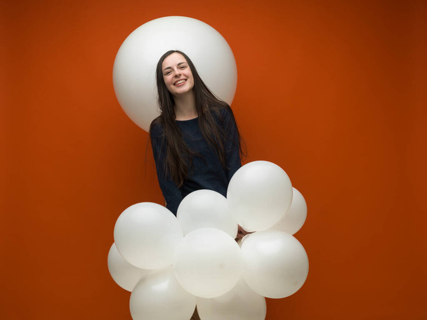 jovem morena com cabelos longos rindo com balões brancos em suas mãos sobre fundo laranja - Foto, Imagem