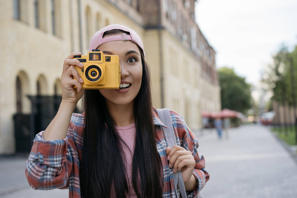Sonriente fotógrafo turístico asiático tomando fotos caminando por la calle. Vacaciones, concepto de viaje, espacio de copia - Foto, Imagen