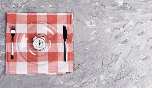 Alarm clock and an empty plate of cutlery. The concept of intermittent fasting, lunch, diet and weight loss - Photo, Image