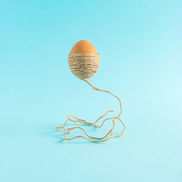 Пасхальное яйцо с коричневой веревкой левитирует в воздухе на синем фоне. Минимальный отпуск или концепция питания. - Фото, изображение