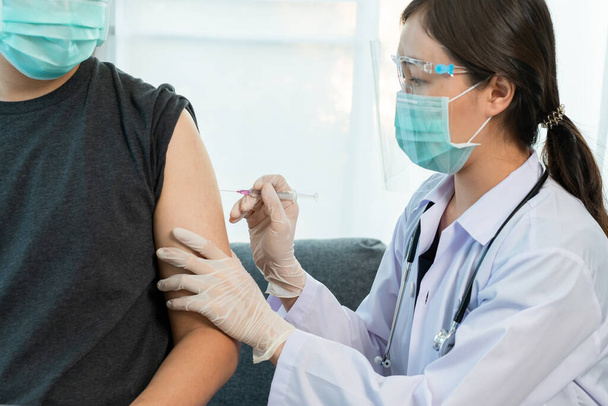 Asian professional doctor injecting a Coronavirus 2019-nCoV or COVID-19 vaccine at male patient arm close up, COVID19 vaccinating about protecting and build antibody - immunity against Coronavirus. - Foto, afbeelding