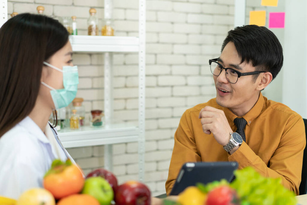 Young Asian man come to meet the nutritionist in hospital and talking about dieting and eating. Expertise nutritionist giving a eating recommendation to a man who have health problem. - Photo, image