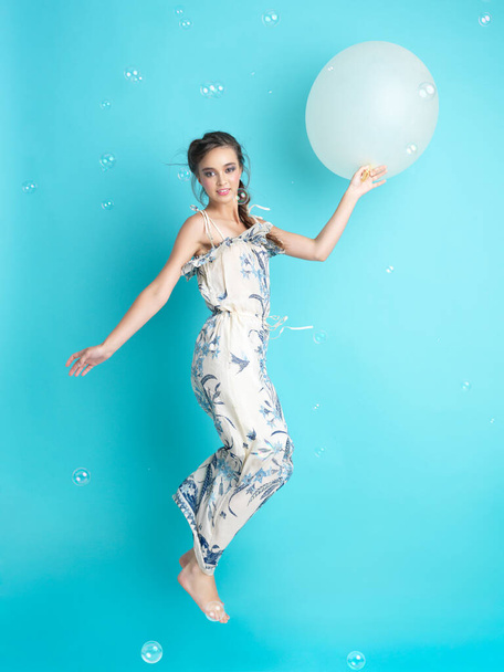 όμορφη, χαρούμενη, νεαρή γυναίκα που πηδάει με ένα φουσκωτό μπαλόνι στο χέρι της, περικυκλωμένη από σαπουνόφουσκες. - Φωτογραφία, εικόνα