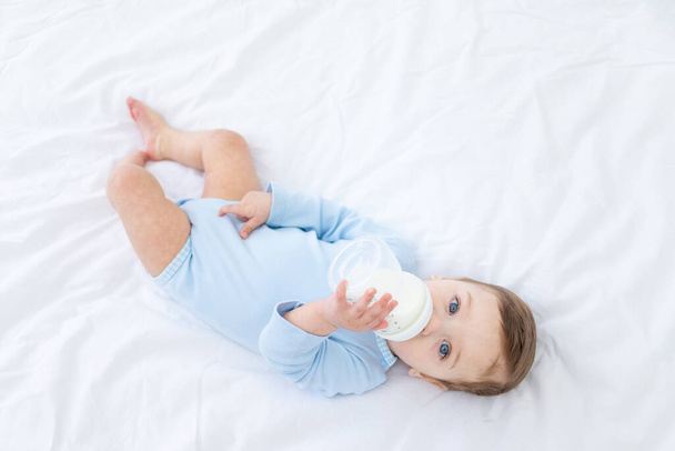baby boy with a bottle of milk on the bed for sleeping in a blue bodysuit, baby food concept - Foto, Imagem