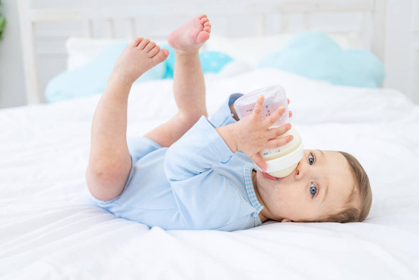 baby boy with a bottle of milk on the bed for sleeping in a blue bodysuit, baby food concept - Foto, afbeelding