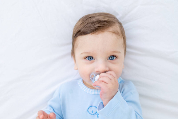 baby boy with pacifier on bed before going to bed in blue bodysuit, happy healthy little baby - Фото, изображение