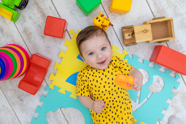 sonriente niño feliz juega en el vivero en un traje de cuerpo amarillo con juguetes de colores brillantes - Foto, Imagen