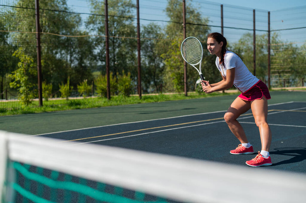 Young caucasian woman playing tennis on an outdoor court on a hot summer day. - Φωτογραφία, εικόνα