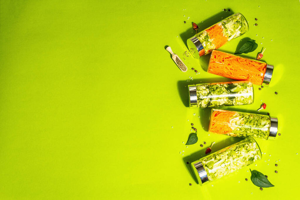 ガラス瓶で健康的な自家製キャベツサラダ。様々なビタミン野菜、スパイス、カトラリーのセット。ビーガン(ベジタリアン)ライフスタイル、トレンディーなハードライト、暗い影。明るい緑の背景、トップビュー - 写真・画像