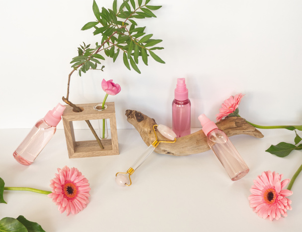Cosmetics spa branding mockups: pink and blue container for tonic or lotion, face roller, sponge on white background. Face care concept. Home spa and bath utensils. Pink flower, green leaf, wooden vase, sea wood, plastic cosmetic bottles - Photo, Image