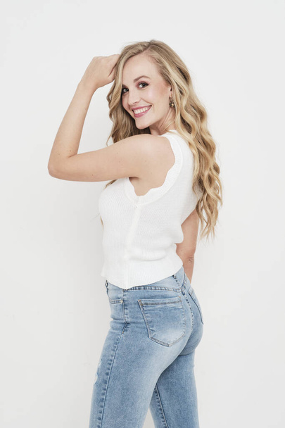 Sexy young blonde girl wearing jeans and a white shirt without sleeves smiling to camera - Fotó, kép