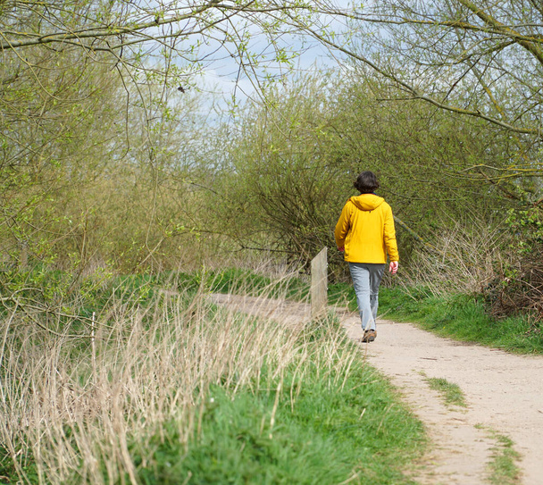 Pessoa em uma jaqueta amarela andando ao longo de um caminho de sujeira - Foto, Imagem