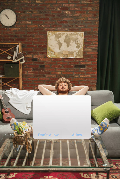 Retrato de un joven con un signo en blanco como pantalla de redes sociales sentado en casa. - Foto, Imagen