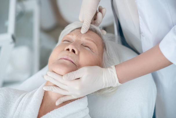 Gray-haired mature woman lying with closed eyes having a face massage - Photo, Image