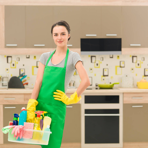 若い幸せな白人女性が台所で掃除用品を持っています - 写真・画像