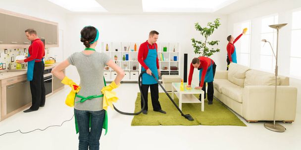 άνδρας καθαρίζει το σπίτι σε διαφορετικά μέρη την ίδια στιγμή ενώ η γυναίκα επιβλέπει την πρόοδο - Φωτογραφία, εικόνα