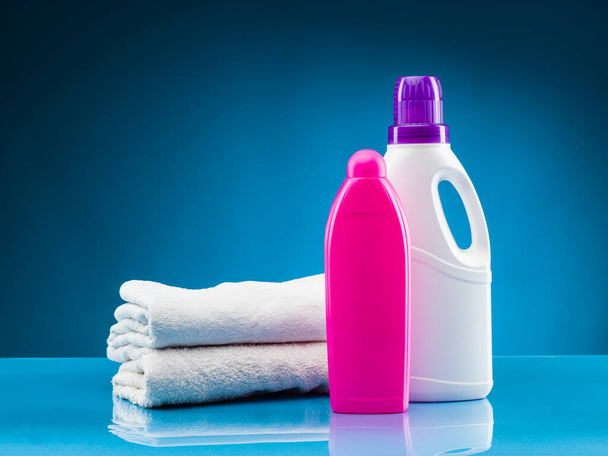weiße Handtücher, flüssiges Waschmittel und Weichspüler vor blauem Hintergrund - Foto, Bild
