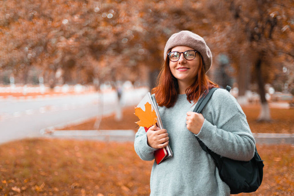 Női tanuló sétál a parkban, alkalmi ruhát visel szemüveggel, jegyzetfüzeteket és könyveket tart a parkban campus - Fotó, kép