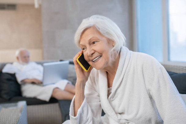 Grijsharige lachende vrouw kijkt blij en praten aan de telefoon - Foto, afbeelding