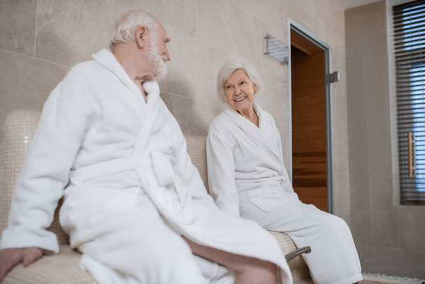 Senior couple in white robes having procedures for legs in spa salon - Фото, изображение