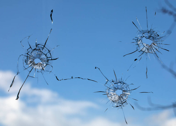 отверстия и трещины от пуль в стекле, на фоне неба, выстрел окон. - Фото, изображение