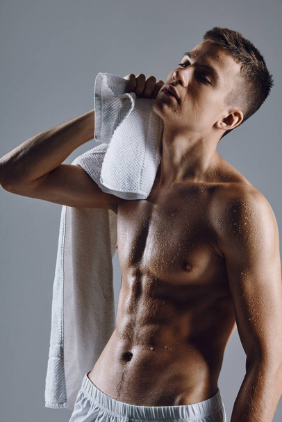 Ένας τύπος με μια πετσέτα στα χέρια του σκουπίζει τους φουσκωμένους κοιλιακούς ενός μπόντι μπίλντερ. - Φωτογραφία, εικόνα