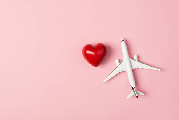 Overhead φωτογραφία του αεροπλάνου και κόκκινη καρδιά απομονώνονται στο ροζ φόντο με κενό χώρο - Φωτογραφία, εικόνα
