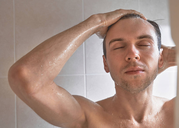 Portret młodego przystojniaka myje się żelem pod prysznic, mieli głowę szamponem w łazience w domu zbliżenie - Zdjęcie, obraz