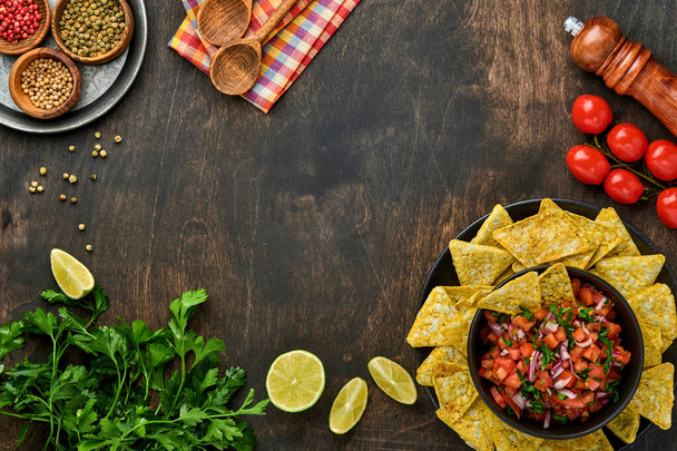 Traditional Mexican tomato sauce salsa with nachos and ingredients tomatoes, chile, garlic, onion on dark old wooden background. Concept of Latin American and Mexican food. Mock up. - Fotó, kép
