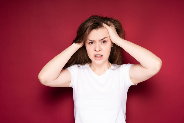 Pretty girl gets annoyed with headache after getting braces. Isolated on red background - Foto, imagen