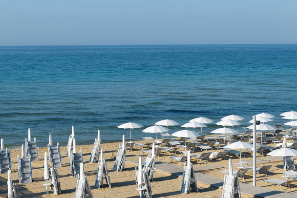 Le matin, parasols sur la plage de Lido di San Pietro à Bevagna près de Mandurie, région des Pouilles, Italie sur fond bleu mer Ionienne - Photo, image