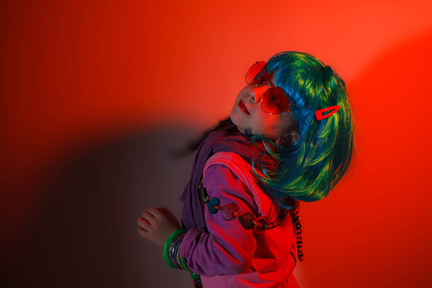 Portrait of a glamour little girl wearing colorful wig on red background - Photo, Image