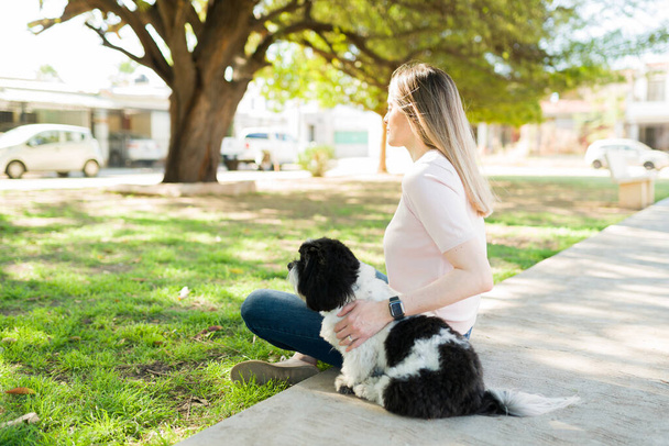隣の忠実な犬と一緒に公園に座っている思慮深い女性。美しい犬の所有者リラックス屋外とともに彼女のshish tzuペット - 写真・画像