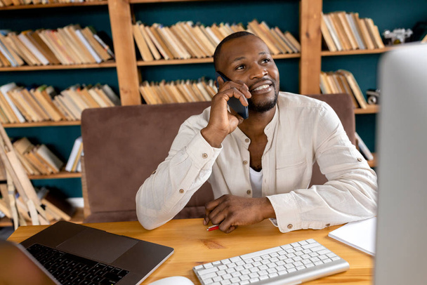 african american businessman sitting at desk and talking on phone - Foto, Bild