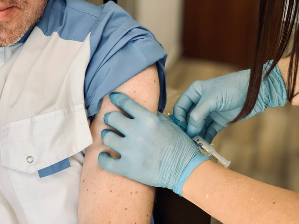 Pacjent otrzymujący szczepionkę przeciw koronawirusowi w klinice. Zbliżenie. Lekarz podaje pacjentowi zastrzyk lub szczepionkę w ramię. Szczepionka przeciwko Covid-19. - Zdjęcie, obraz