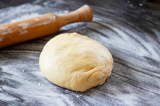 Φρέσκια ζύμη έτοιμη για ψήσιμο. Ζύμη ψωμιού σε ξύλινο πάγκο κουζίνας με πλάστη. - Φωτογραφία, εικόνα