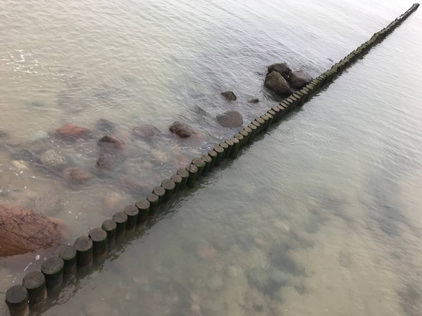 Σπάσιμο κυμάτων σε ένα ξύλινο κυματοθραύστη στις ακτές της Βαλτικής Θάλασσας. - Φωτογραφία, εικόνα