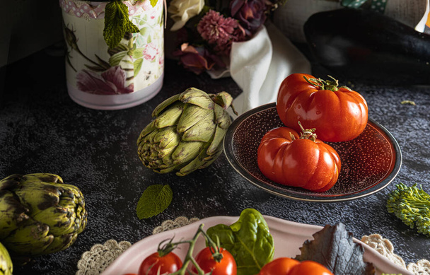 Moody dark food photography of fresh raf tomatoes, bimi and artichokes. Still life image with a vintage look and a black background. - Фото, зображення