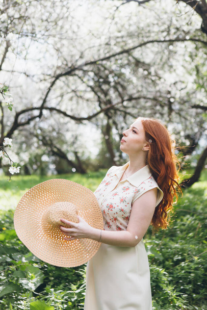 Young beautiful red-haired girl walks in a spring blooming apple orchard. Tinting. - Foto, Imagem