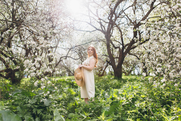 Young beautiful red-haired girl walks in a spring blooming apple orchard. Tinting. - Foto, Bild