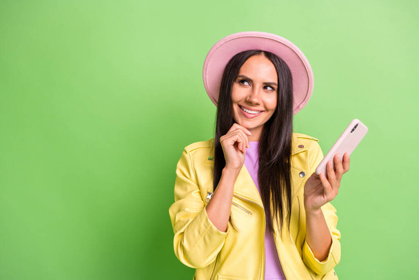 Photo of lovely lady hold cellphone look empty space wear yellow jacket pink headwear isolated green color background - Photo, image