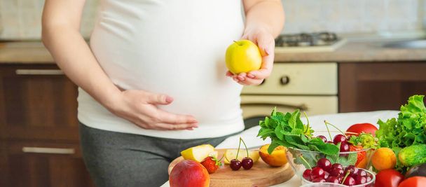 Eine schwangere Frau isst Gemüse und Obst. Selektiver Fokus. Lebensmittel. - Foto, Bild