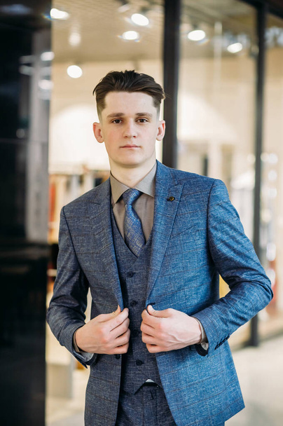 A charming person. Handsome young man in suit looking at camera and straightening jacket while standing indoors - Fotografie, Obrázek