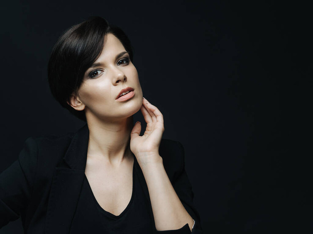 Portrait of sensual woman with short haircut and light makeup standing over black background. Charming confident lady wearing black elegant clothes. - Foto, Imagem