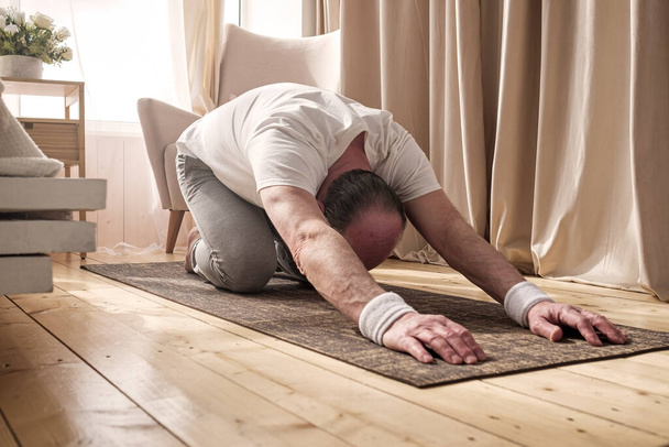 Active senior man doing the child pose while practicing yoga on a mat - Valokuva, kuva