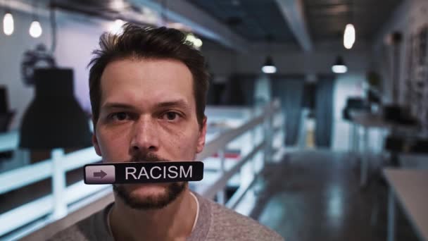 Mann blickt in die Kamera und hält ein Schild mit der Aufschrift RACISMUS in den Mund - Filmmaterial, Video