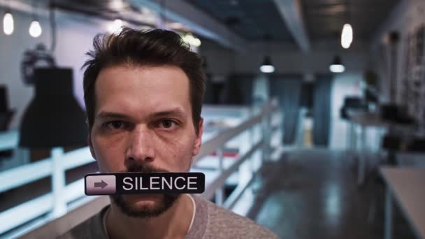 Мужчина смотрит в камеру и держит во рту табличку с надписью SILENCE - Кадры, видео